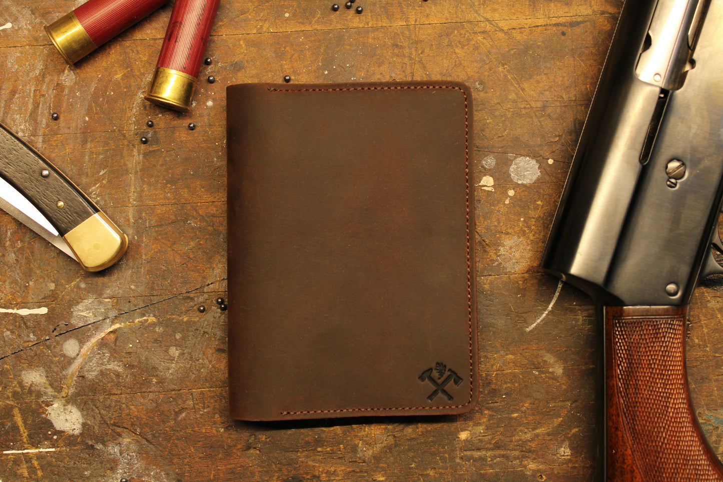 Closed leather notebook holder with pocket knife and shotgun shells on wood