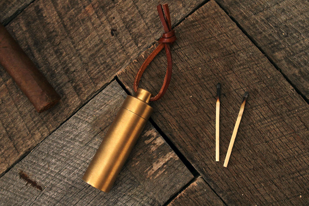 Brass match holder next to two matches on grey wood