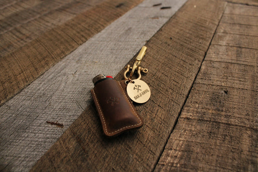 Leather lighter sleeve with Oak And Anvil logo and brass keychain on grey wood