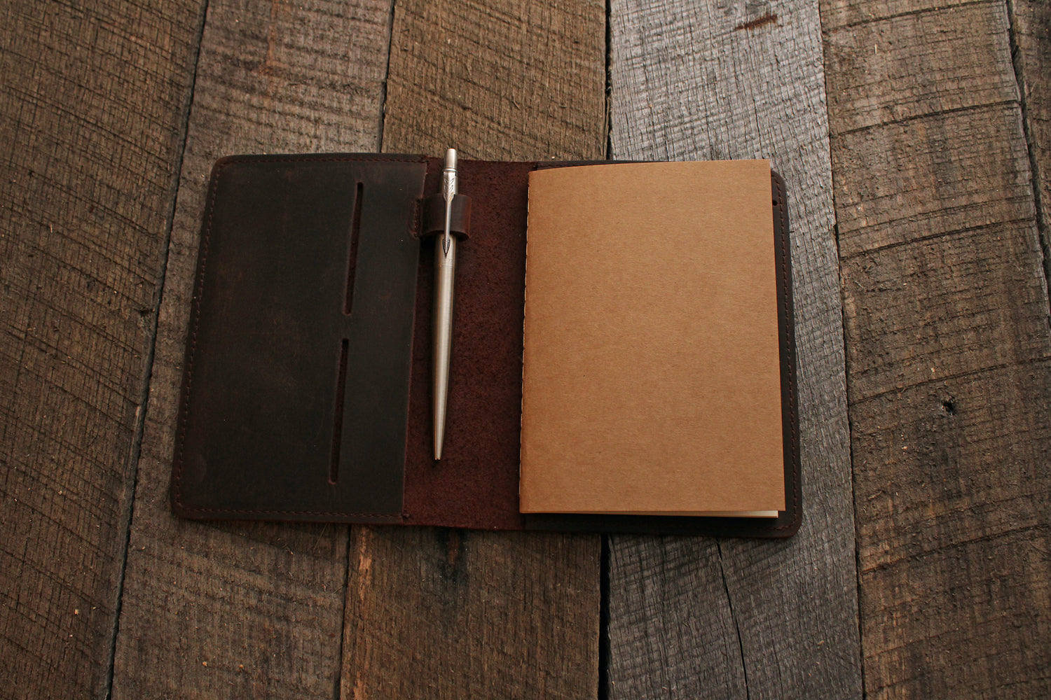 Open leather notebook holder with silver pen on grey wood 