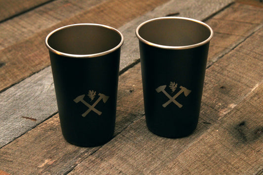 Two matte black stainless steel cups with Oak and Anvil logo on wood