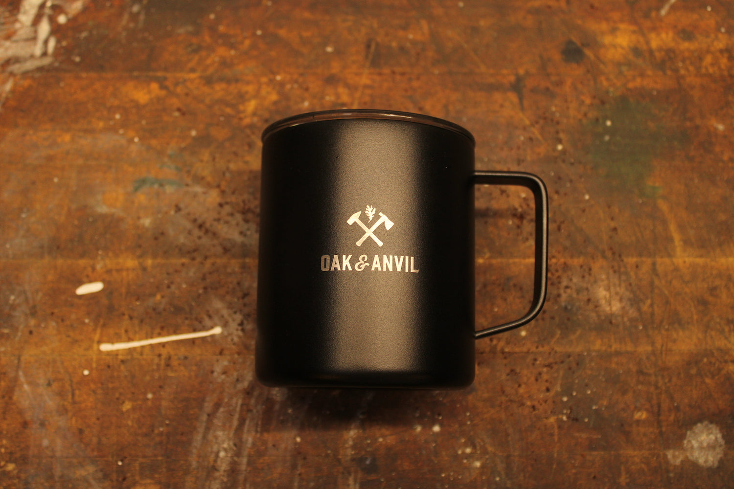 Black stainless steel insulated mug with Oak and Anvil logo laying on wood